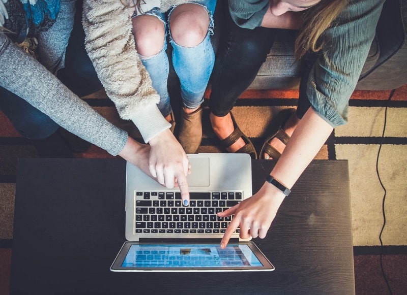 3 people pointing their hands on a laptop.