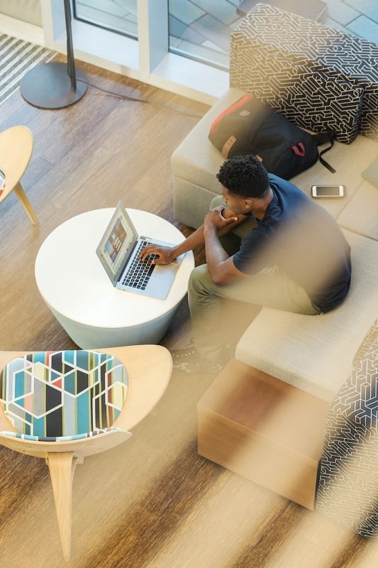 Man sitting on a sofa and using his laptop for the Facebook campaign setup targeting.