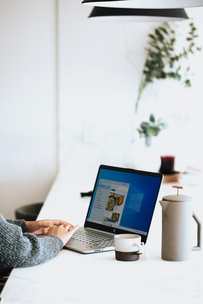 Laptop place on top of a table along a cup and a pitcher.